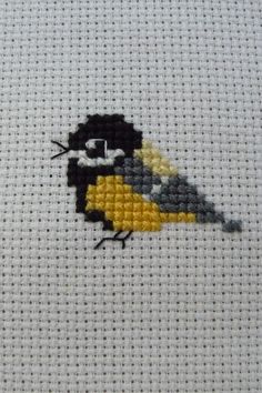 a small cross stitch bird sitting on top of a white table cloth with black and yellow accents