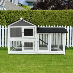 a chicken coop in the grass next to a white picket fence and some houses with windows