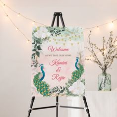 a welcome sign is on an easel next to a vase with flowers and greenery