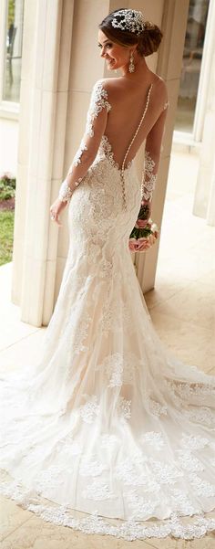 a woman in a wedding dress is looking at the back of her gown, which has an open shoulder and long sleeves