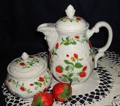 two strawberry covered teapots sitting on top of a doily