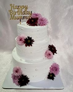 a three tiered white cake with purple flowers on the side and happy birthday mum written on top