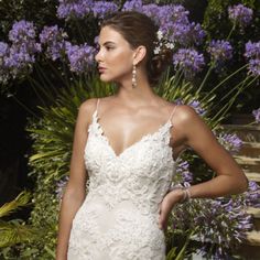 a woman in a wedding dress standing next to purple flowers