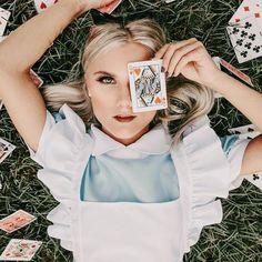 a woman laying in the grass with playing cards on her head and hands over her eyes