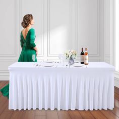 a woman in a green dress sitting at a table with two plates and wine bottles