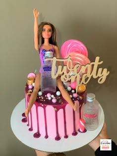 a barbie doll sitting on top of a pink cake with purple icing and sprinkles