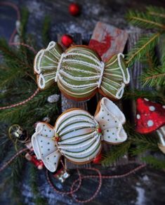 three decorated cookies sitting on top of a wooden table next to christmas tree branches and decorations