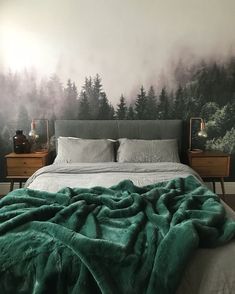 a bed with green sheets and pillows in front of a forest wall mural