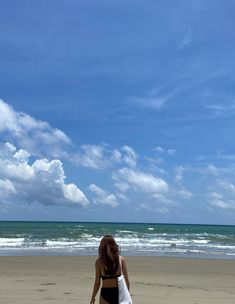 a woman is walking on the beach with her surfboard in hand and looking at the ocean