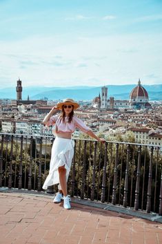 a woman standing on top of a balcony next to a fence and wearing a hat