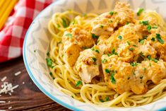 a white bowl filled with chicken and pasta on top of a table next to a red checkered napkin