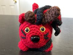 a crocheted red and black stuffed animal with big eyes on top of a table