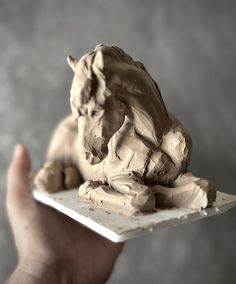 a hand holding a small sculpture of a dog on a plate in front of a gray background