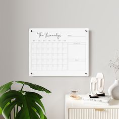 a calendar hanging on the wall next to a potted plant and white vases