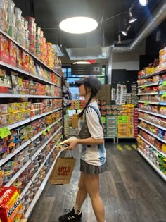 a woman is walking through a grocery store aisle holding a shopping bag and looking at the food shelves