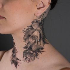 a woman's neck is adorned with black and white roses, leaves and feathers