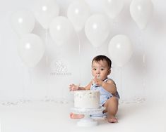 a baby sitting in front of a cake with white balloons