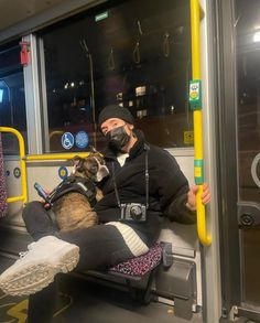 a man sitting on a bus with his dog and wearing a face mask while looking out the window