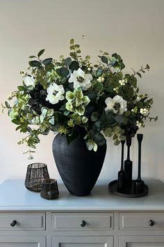 a black vase with white flowers sitting on top of a dresser