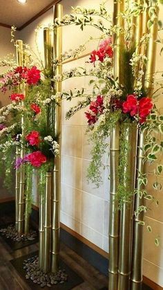 three tall gold vases with red flowers and greenery in them on the floor