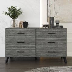 a gray dresser sitting in a living room next to a painting and vases on top of it