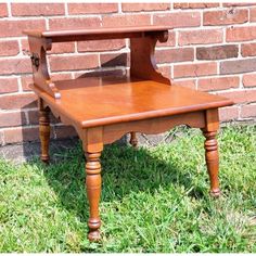 a small wooden table sitting on top of green grass next to a red brick wall