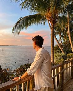 a man standing on a balcony looking out at the ocean with palm trees in the foreground