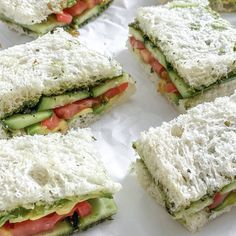 several sandwiches with cucumber, tomato and cheese on white paper lined up next to each other