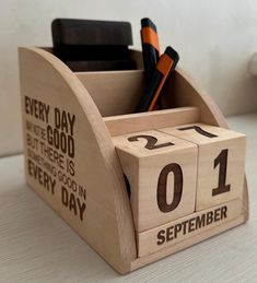 a wooden calendar holder with pens and pencils in it