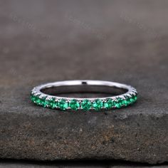 a wedding band with emeralds and white diamonds on top of a stone slabd surface