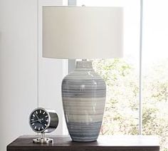 a lamp sitting on top of a wooden table next to a vase with a clock