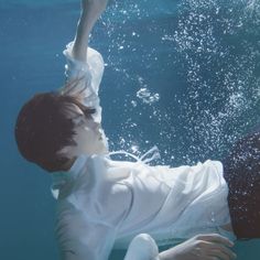 a boy in white shirt under water with his hand up to the sky above him