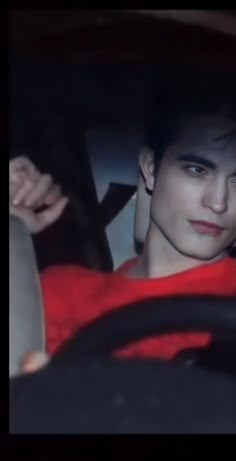 a young man sitting in the driver's seat of a car, looking at the camera