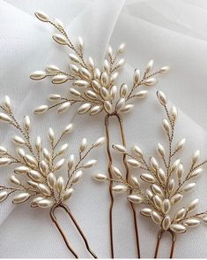 three hair pins with pearls on them sitting on top of a white cloth covered table