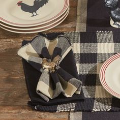 a place setting with black and white plates, napkins and rooster figurines