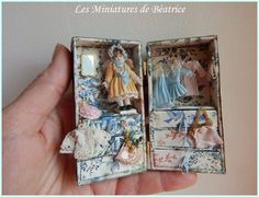 a hand holding an open miniature box with dolls in it's sides and clothes on the inside