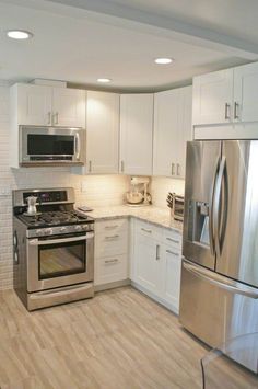 a kitchen with white cabinets and stainless steel appliances in the center, along with hardwood flooring