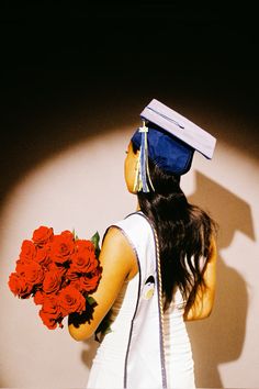 a woman wearing a graduation cap and gown holding a bouquet of red roses in her hand