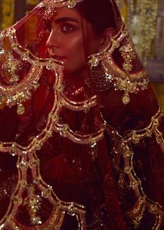 a woman in a red and gold bridal outfit with her veil draped over her head