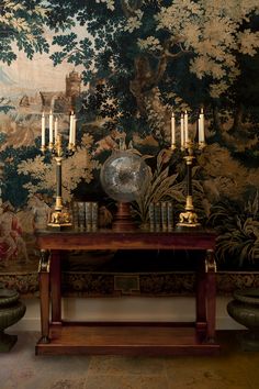 a table with some candles on it in front of a wallpapered background and two urns