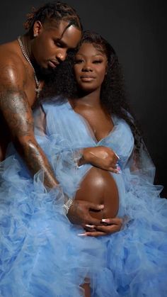 a pregnant woman in a blue dress with her arm around the belly of a man