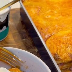 a large casserole dish with cheese and meat in it next to a cup of coffee