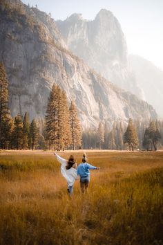 two people are running through a field with mountains in the background