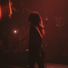 a woman standing in front of a microphone on stage with red light coming from behind her