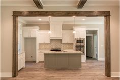 an empty kitchen with white cabinets and wood beams on the ceiling is seen from across the room