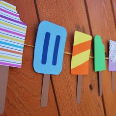 popsicles are lined up on the clothesline to be decorated with colorful paper strips