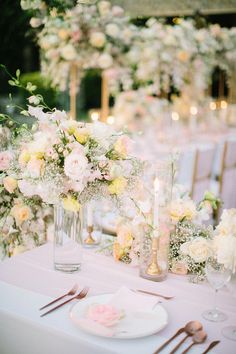 the table is set with white and pink flowers in vases, silverware, and candles