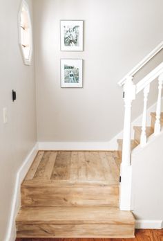 an empty room with stairs and pictures on the wall above it, along with hardwood flooring