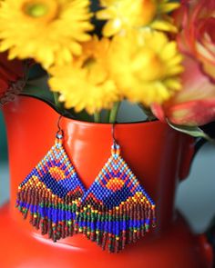 a red vase filled with yellow flowers and colorful beaded earrings