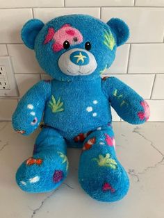 a blue teddy bear sitting on top of a white tile counter next to a wall